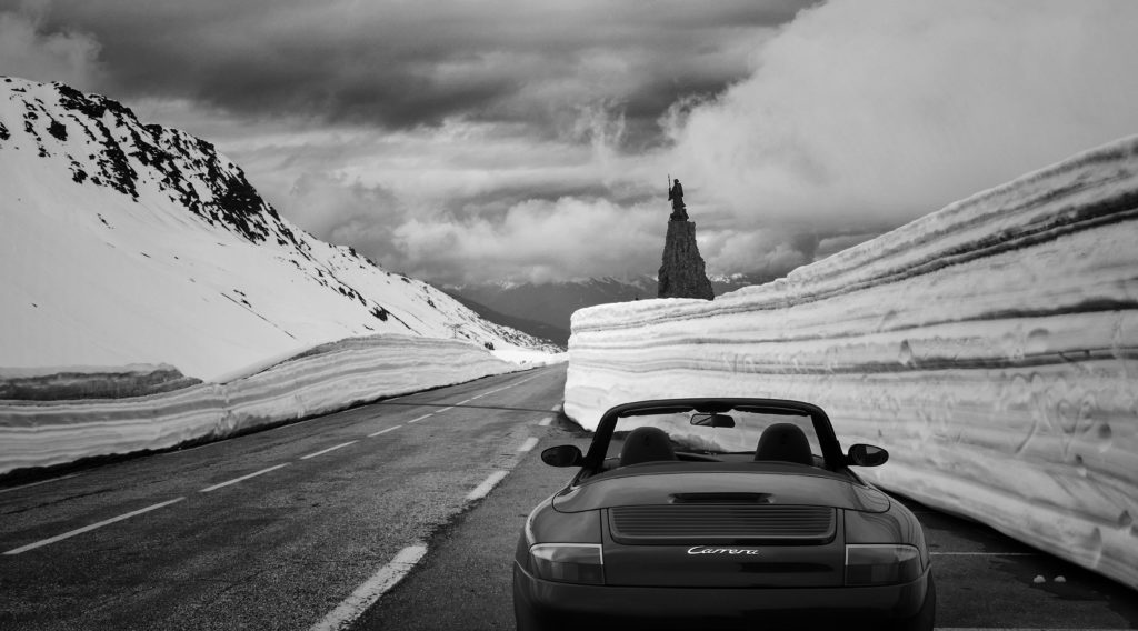 Porsche carerra på fjellvei på vårføre. Store snøvegger på hver side av veien.